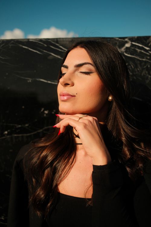 Free A woman in black enjoys the sunlight with eyes closed, reflecting relaxation. Stock Photo