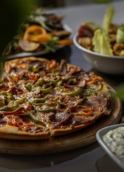 Tasty pizza with peppers and sausage on a wooden board surrounded by various side dishes.