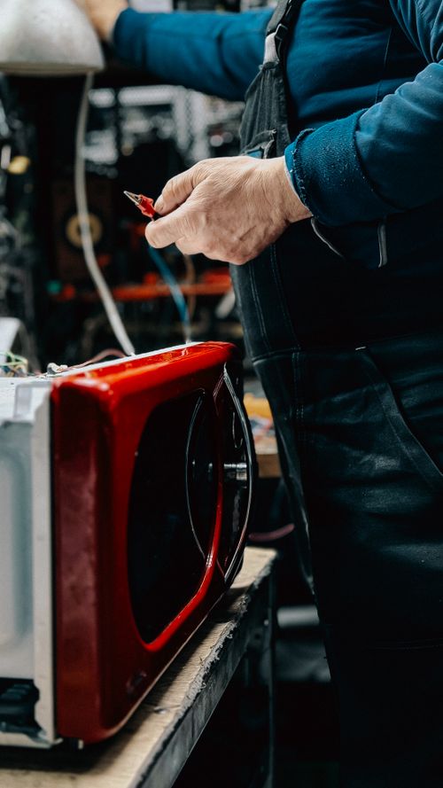 Technician repairing a microwave appliance in a workshop