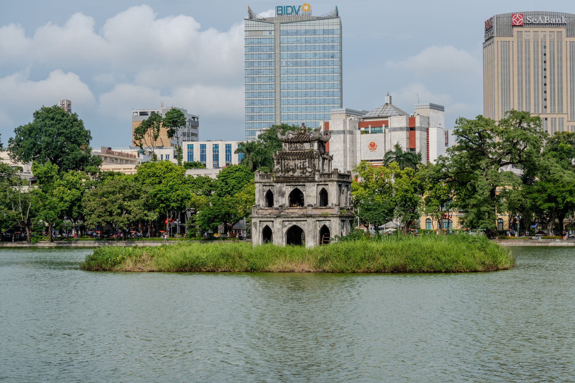Scenic view of Turtle Tower on Hoan Kiem Lake with Hanoi's cityscape backdrop.
