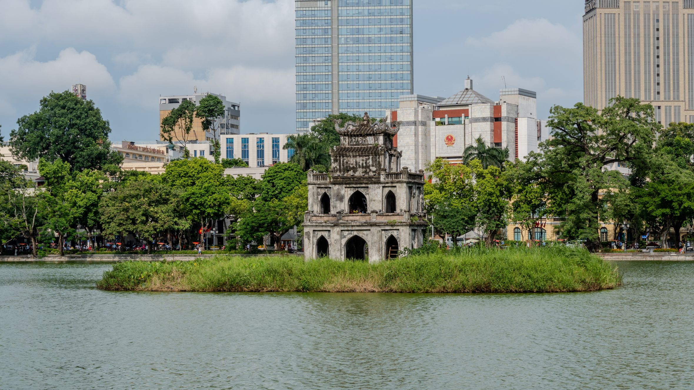 Scenic view of Turtle Tower on Hoan Kiem Lake with Hanoi's cityscape backdrop.