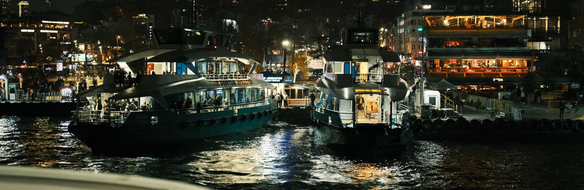 Illuminated boats in a lively harbor at night, showcasing vibrant city nightlife.