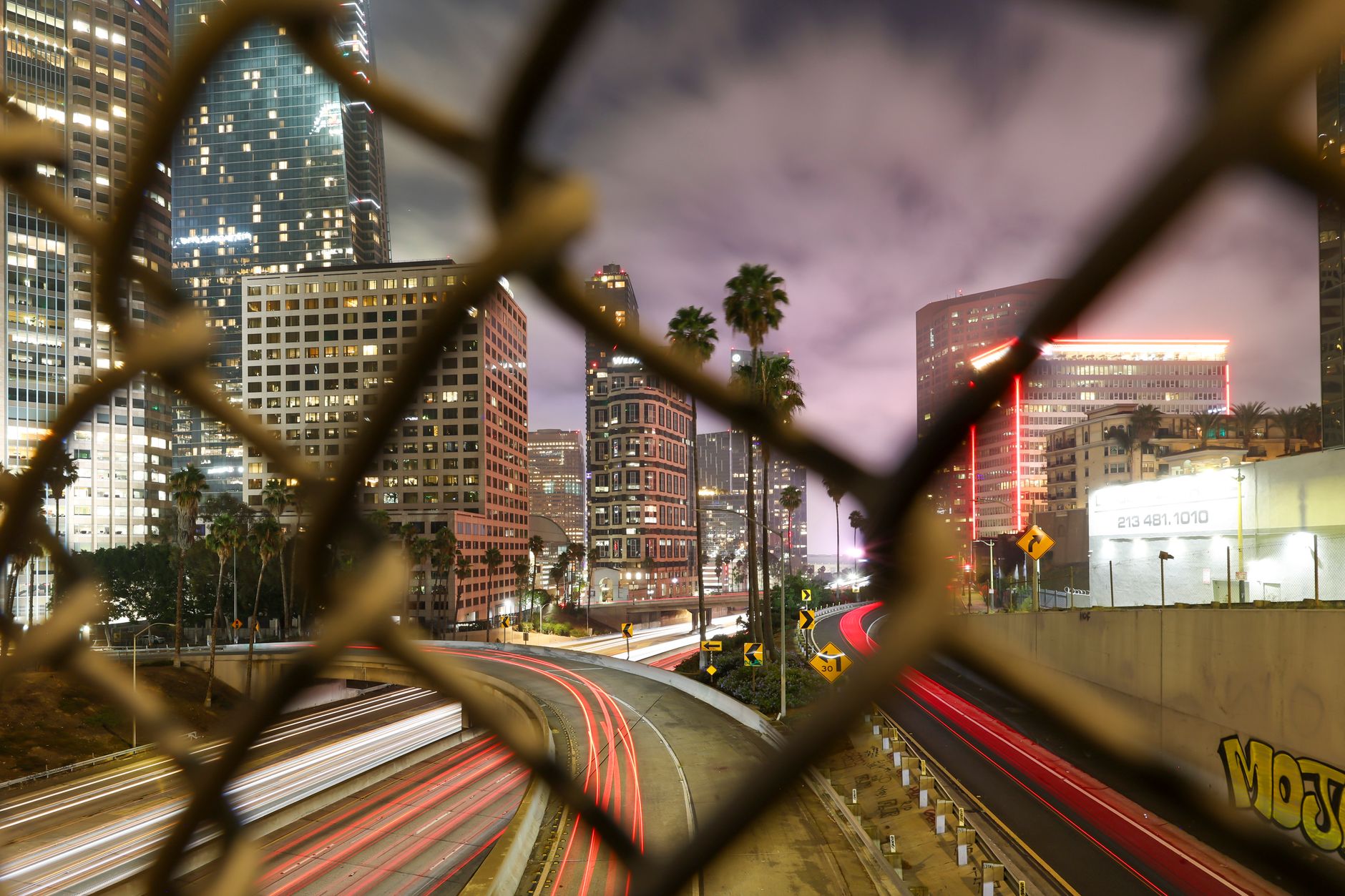 Los Angeles traffic flowing beneath stadium lights while fans navigate signs toward separate World Cup venues