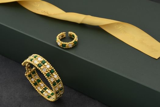 Sophisticated gold bracelet and ring set with green and white gemstones on a dark background.