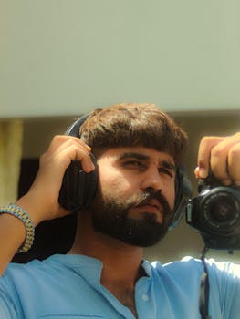 A young man with headphones posing with a camera outdoors in Pakistan.