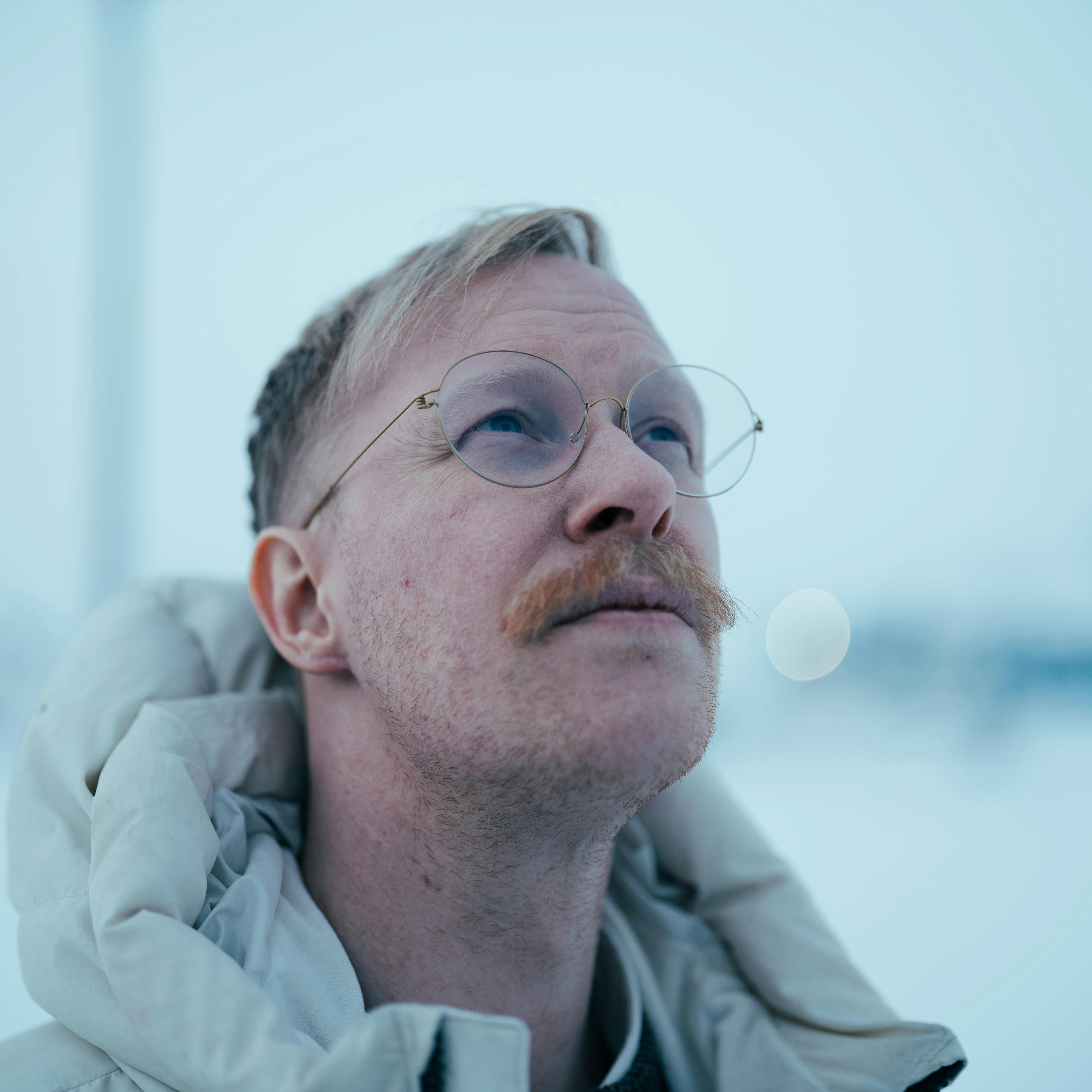 Kostnadsfria Porträtt av en man med glasögon och mustasch som tittar uppåt i snöiga Nuuk, Grönland under vintern. Stock foto