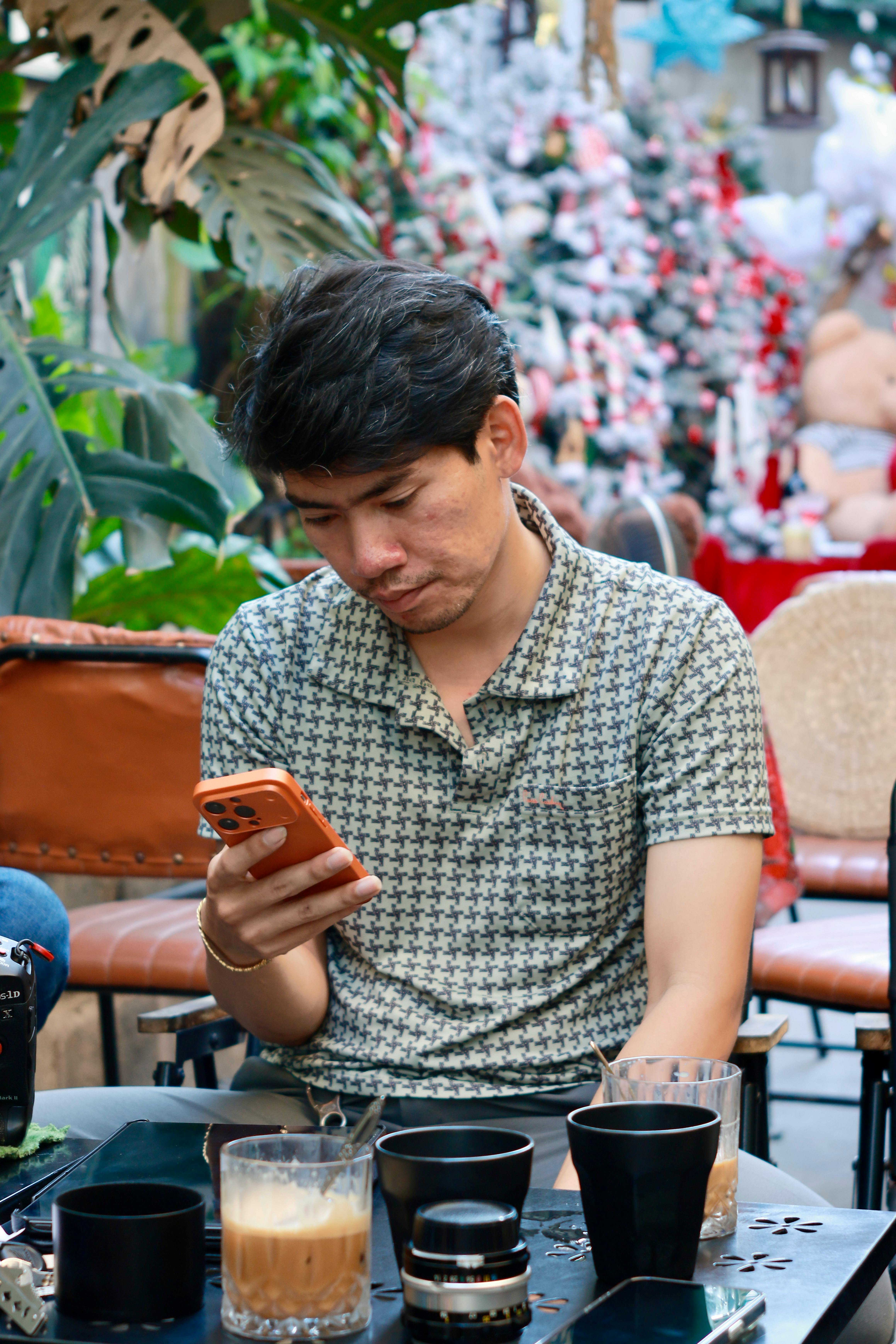grátis Homem vestido casualmente checando o celular em um café com decoração natalina. Foto profissional