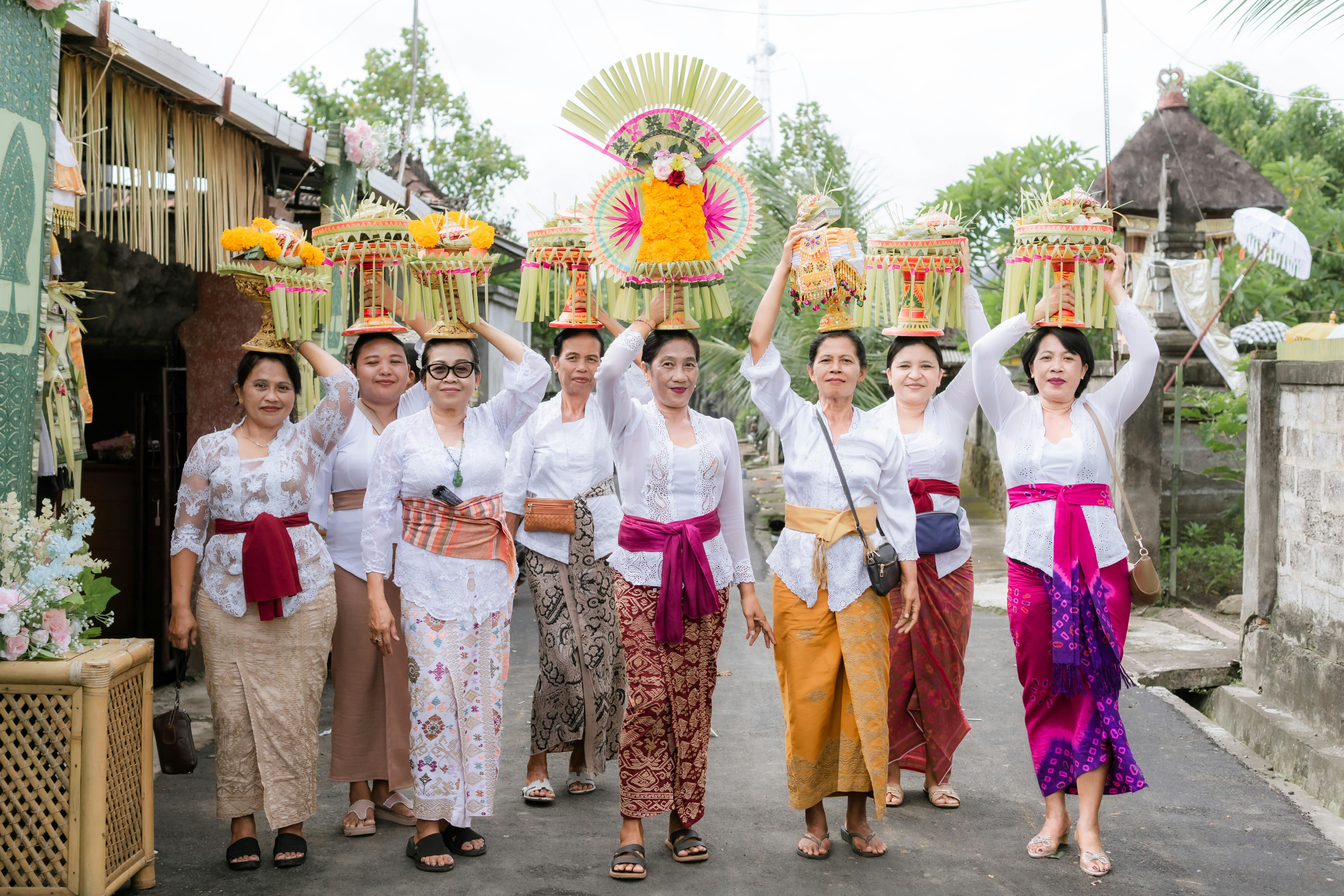 Balinese Hindu women in traditional dress carrying tall offerings of fruit and flowers to a temple ceremony in Bali