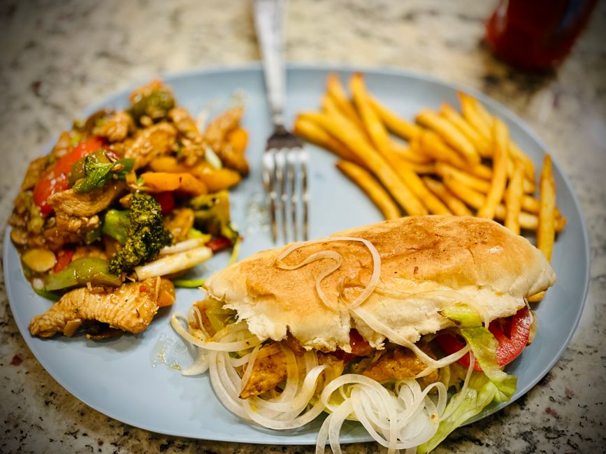 A crusty roll piled high with shredded sofrito-braised chicken, lettuce, tomato, and avocado, cut in half to show the filling.