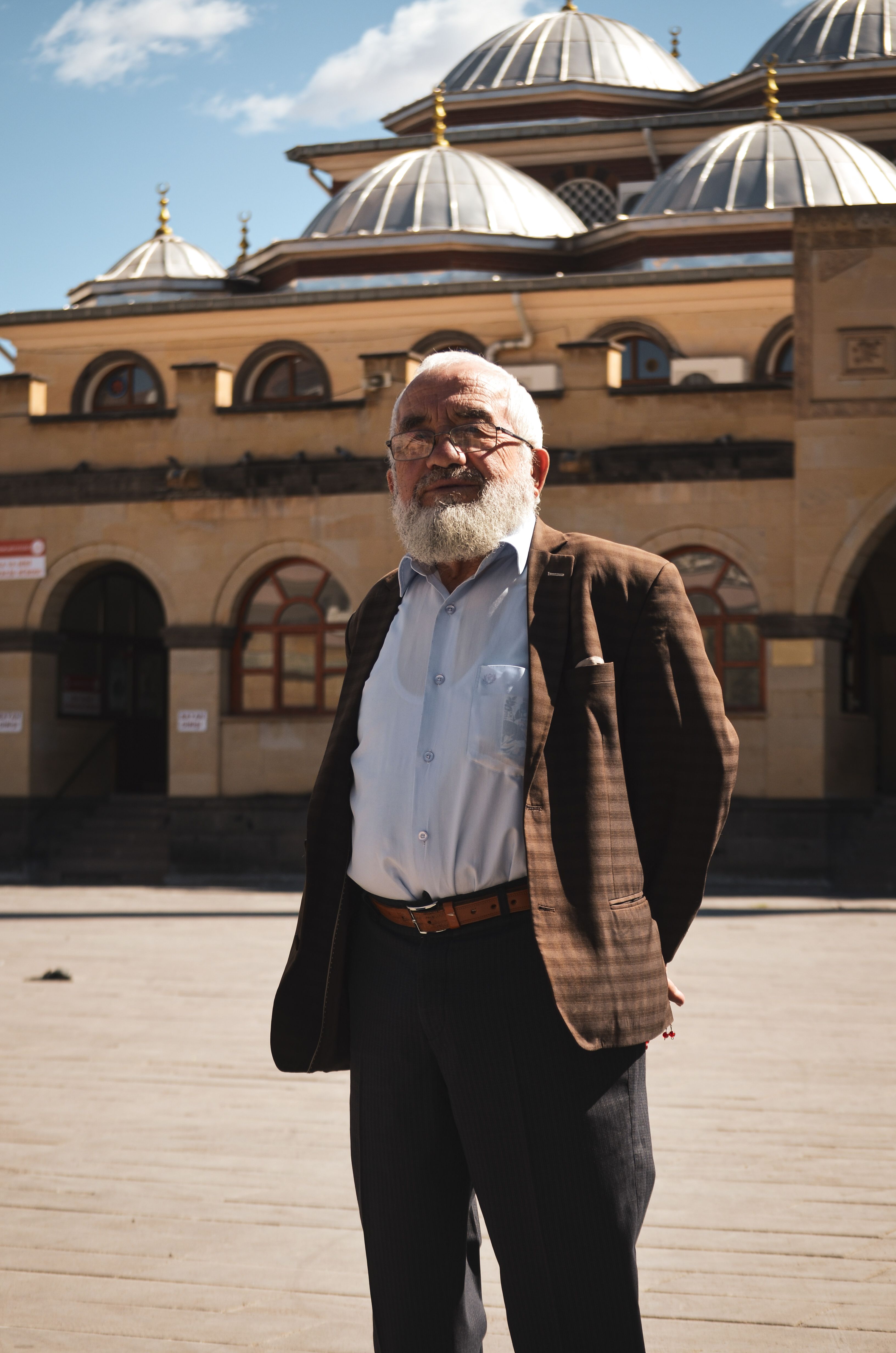 Senior man stands confidently in front of a historic building in Çankırı, Türkiye on a sunny day.