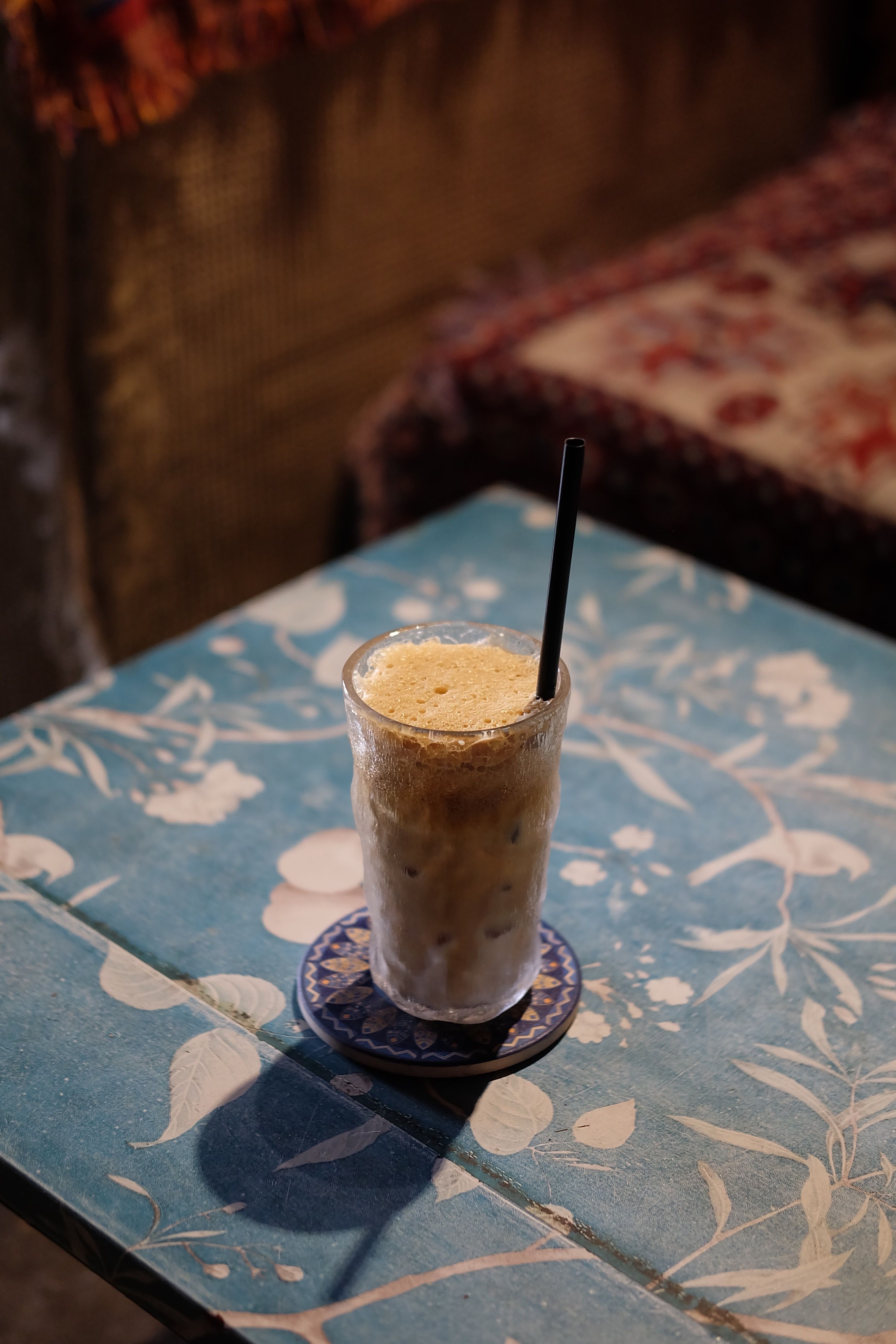 Iced coffee on floral table in a cozy vintage cafe with warm lighting.