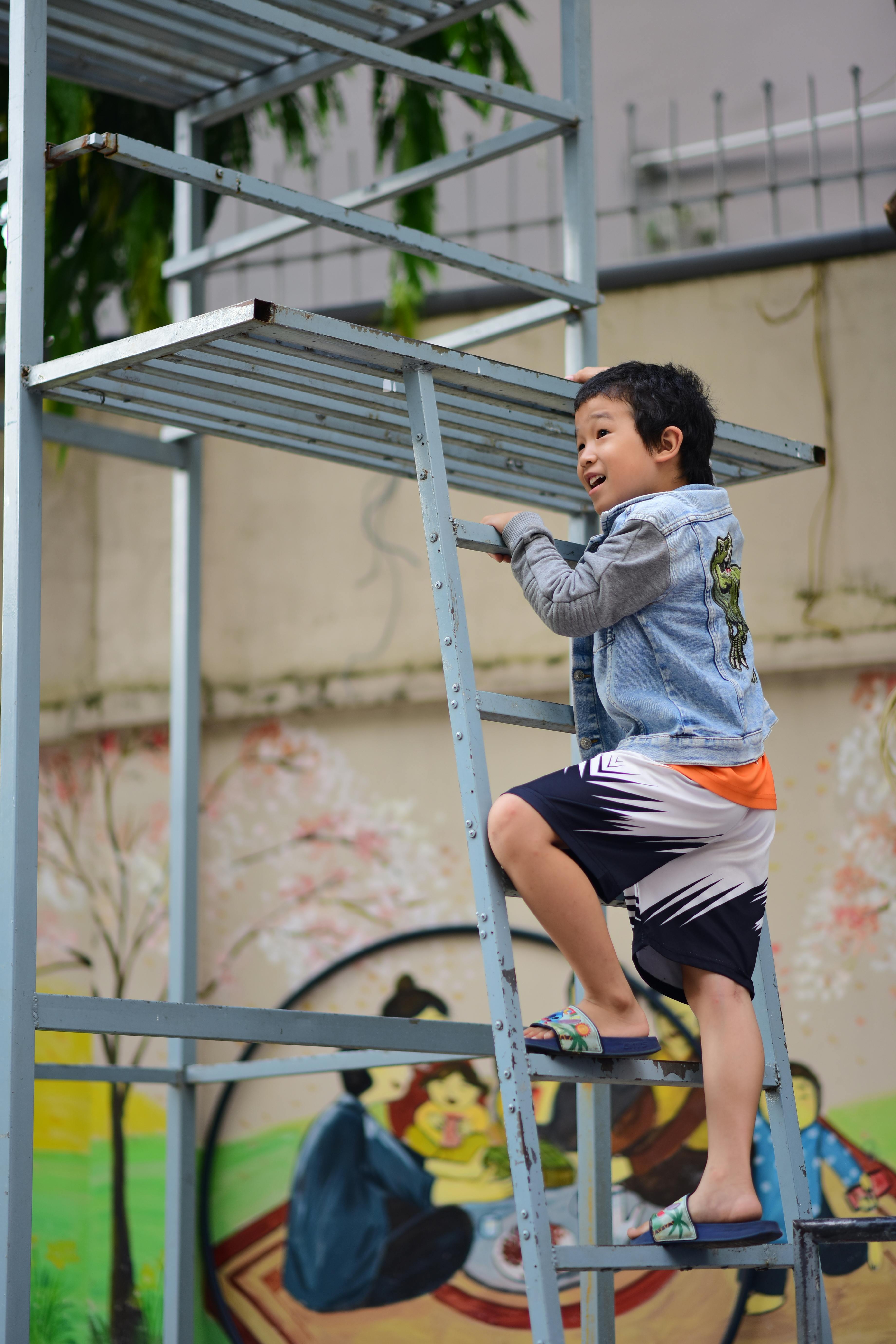 Young boy climbing a metal structure outdoors with a mural in the background.