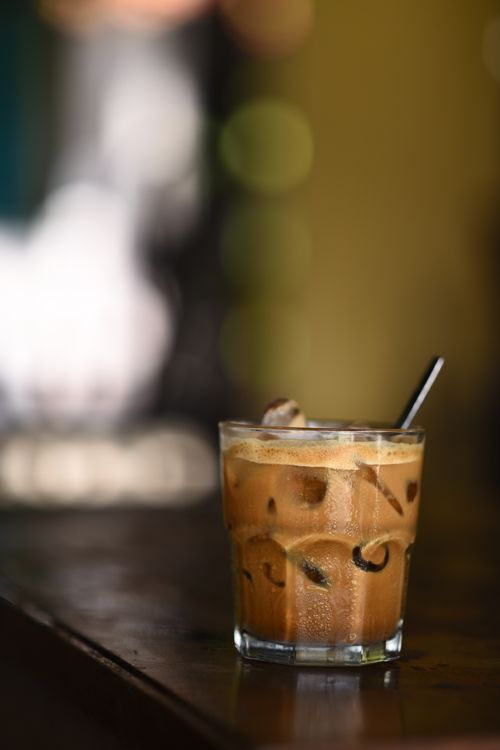 Free Close-up of a frothy iced coffee in a glass on a rustic wooden bar with warm ambient lighting. Stock Photo