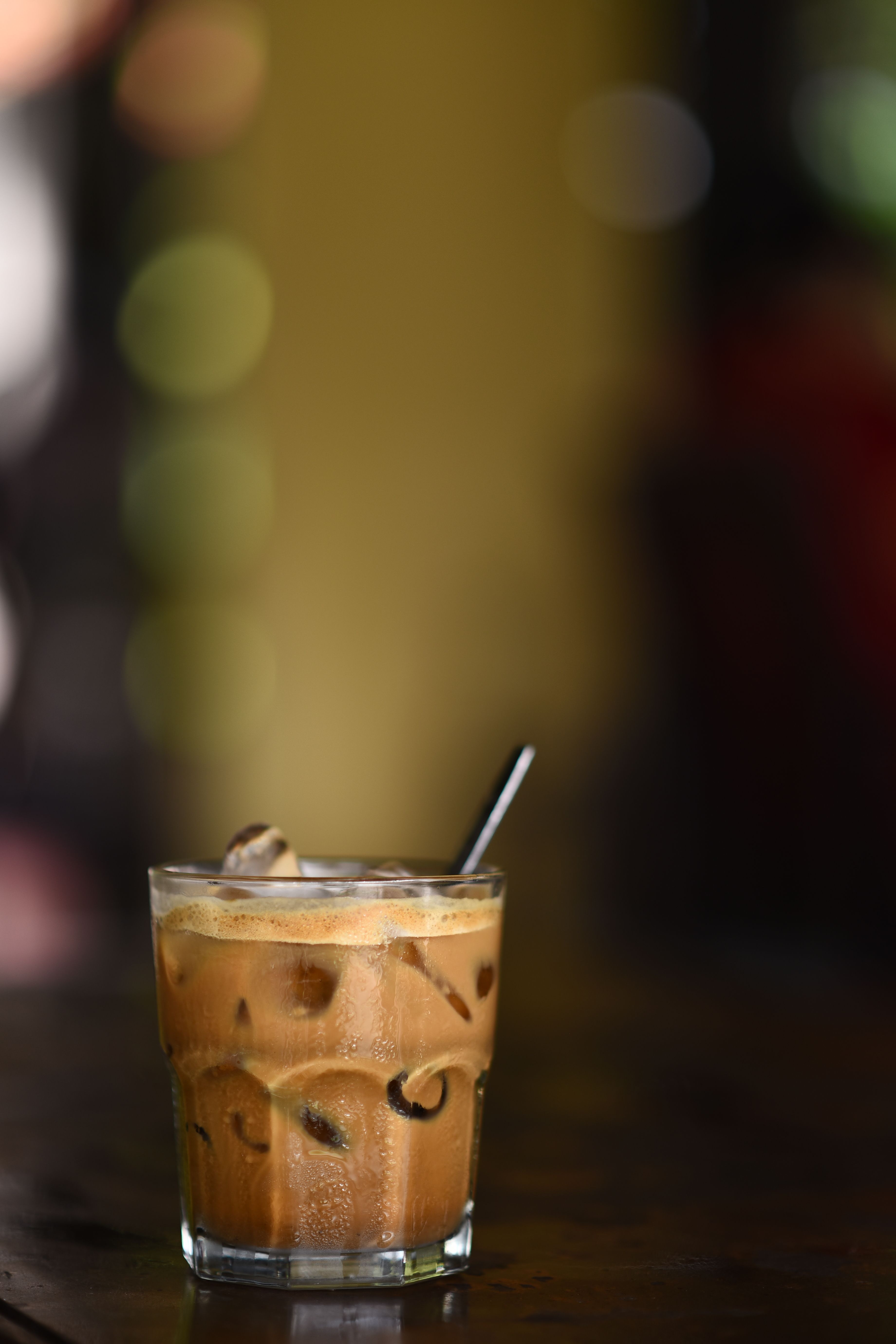A glass of iced coffee with milk on a dark wooden table in a cozy indoor setting.