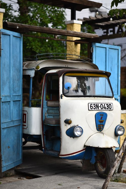 Free A charming vintage tuk-tuk parked inside a rustic garage with blue doors. Stock Photo