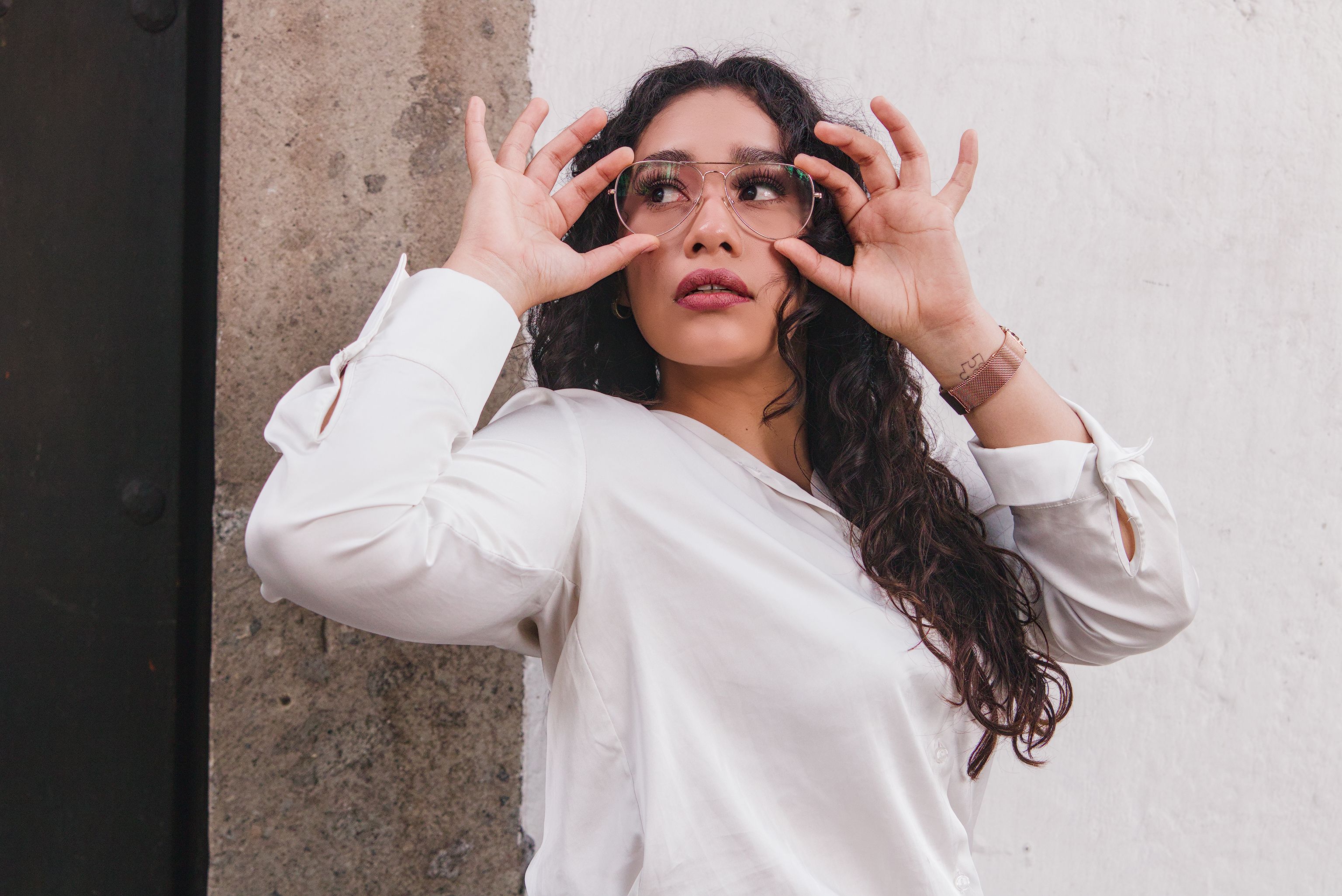 Stylist adjusting sunglasses against a plaster wall, photo by Evoking Ephemerality on Pexels
