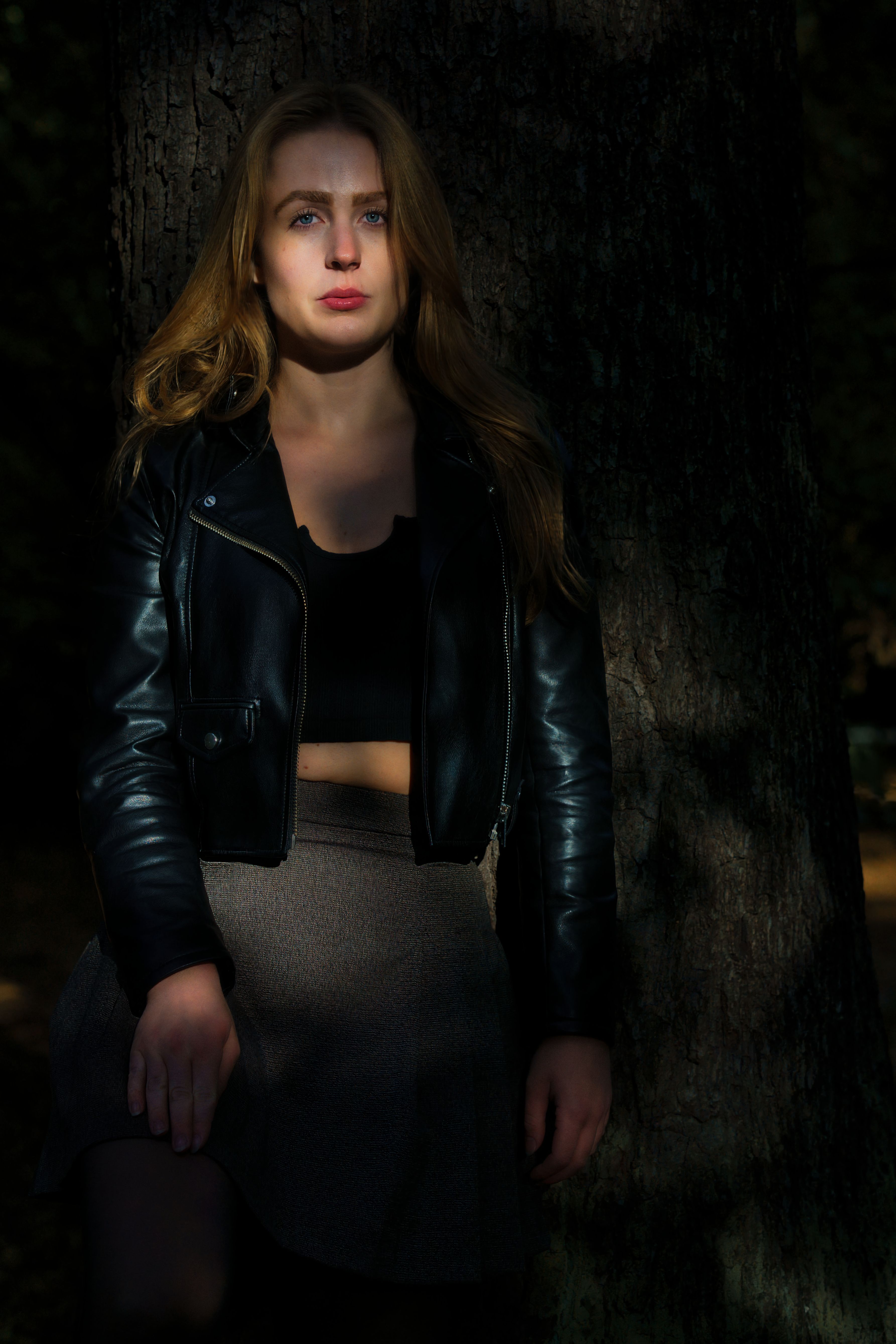 Portrait of a woman in leather jacket against a tree in Berlin. Dramatic lighting and autumn setting.
