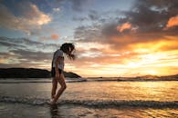 一名女子沿着海滩散步，在充满活力的日落中，海浪轻轻地拍打着她的脚