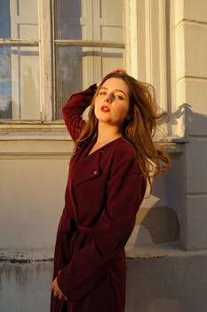 A fashionable woman poses confidently by a window in Berlin during sunset.