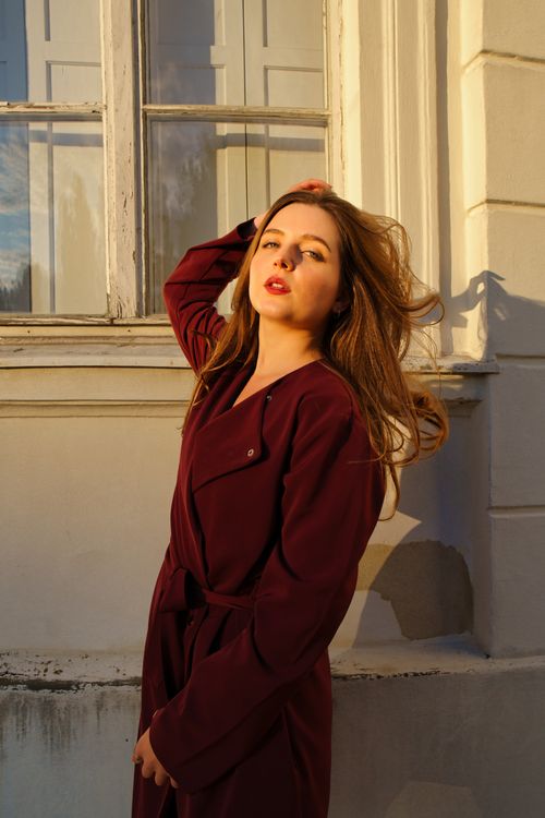 Free A fashionable woman poses confidently by a window in Berlin during sunset. Stock Photo