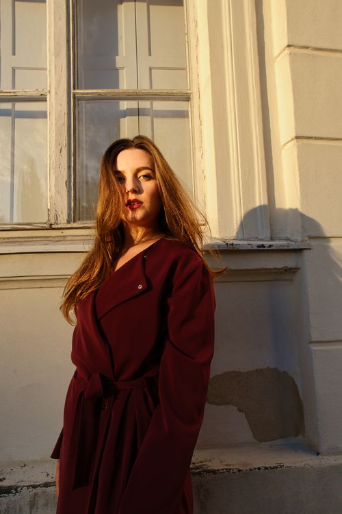 Free Portrait of a woman in a burgundy coat leaning against a building in Berlin, Germany. Stock Photo