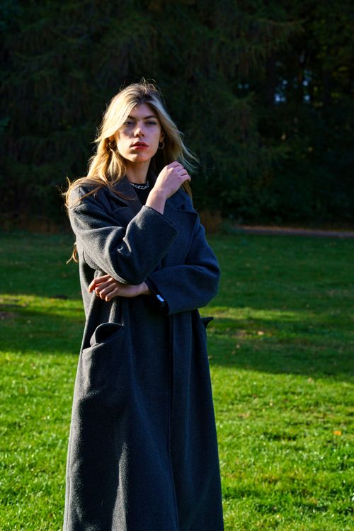 Free Elegant woman in a long coat standing confidently in a park in Berlin during daytime. Stock Photo