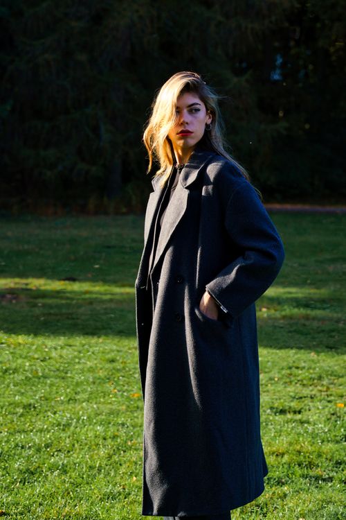 Free A fashionable woman photographed in a Berlin park, showcasing a long dark coat in the autumn sunlight. Stock Photo