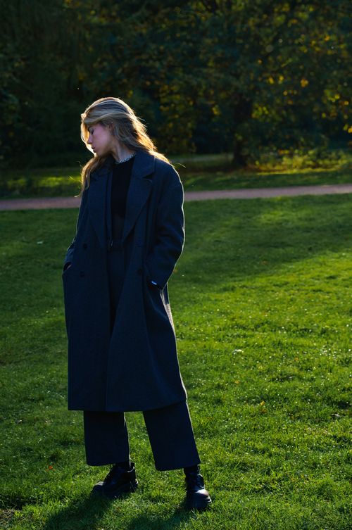 Free Stylish woman in dark attire stands gracefully on green grass in a Berlin park under dappled sunlight. Stock Photo