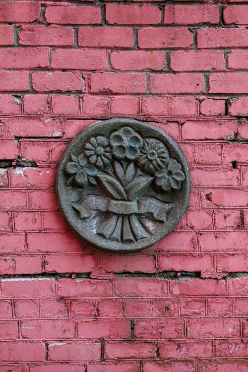 Free Rustic floral carving on a textured pink brick wall, outdoor decor. Stock Photo