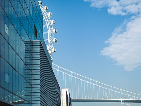 Contemporary architecture with a Ferris wheel and bridge under a clear blue sky.