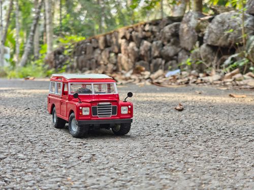 Free A red toy car sits on a rural road with a stone wall background. Stock Photo