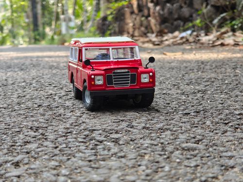 Free A vibrant red toy car on a textured road with a natural outdoor background. Stock Photo
