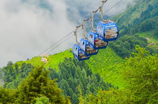 Breathtaking view of cable cars gliding over lush green mountainous landscape with mist.