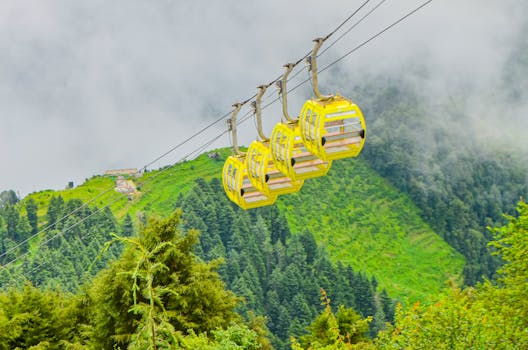 Yellow gondolas glide over lush, misty green mountains, creating a serene travel experience.