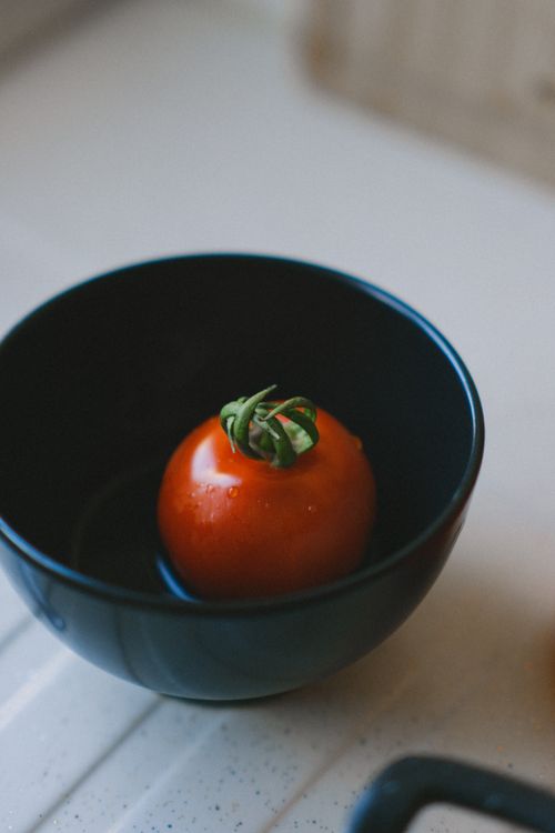 Free A fresh tomato sits alone in a black bowl on a kitchen surface. Stock Photo