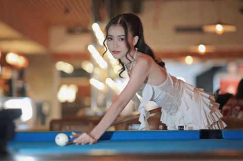 Free Sophisticated woman in white dress playing pool indoors. Stylish bar setting with ambient lighting. Stock Photo
