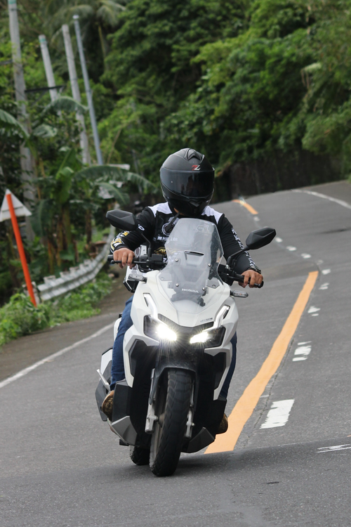 Free A person riding a motorcycle on a winding mountain road surrounded by lush greenery. Stock Photo