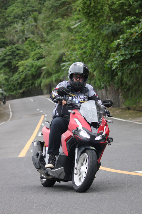 Free Motorcyclist on a red bike rides through a lush, scenic mountain road. Stock Photo