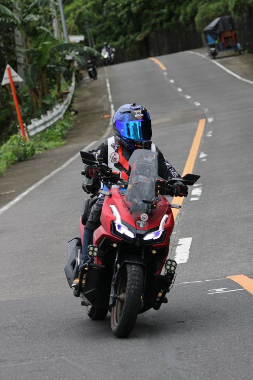 Free Motorcyclist with reflective helmet drives on a winding mountain road, showcasing adventure and freedom. Stock Photo