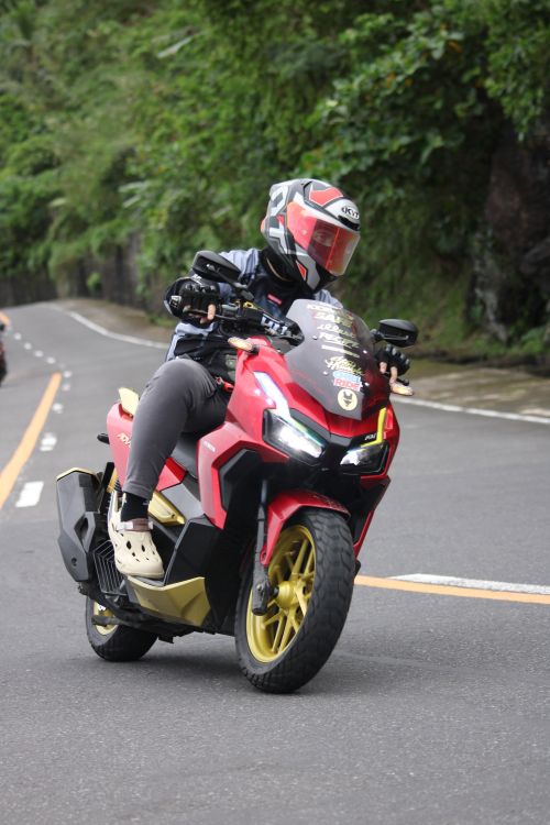 Free Rider on a red motorcycle turning on a scenic mountain road with lush greenery. Stock Photo