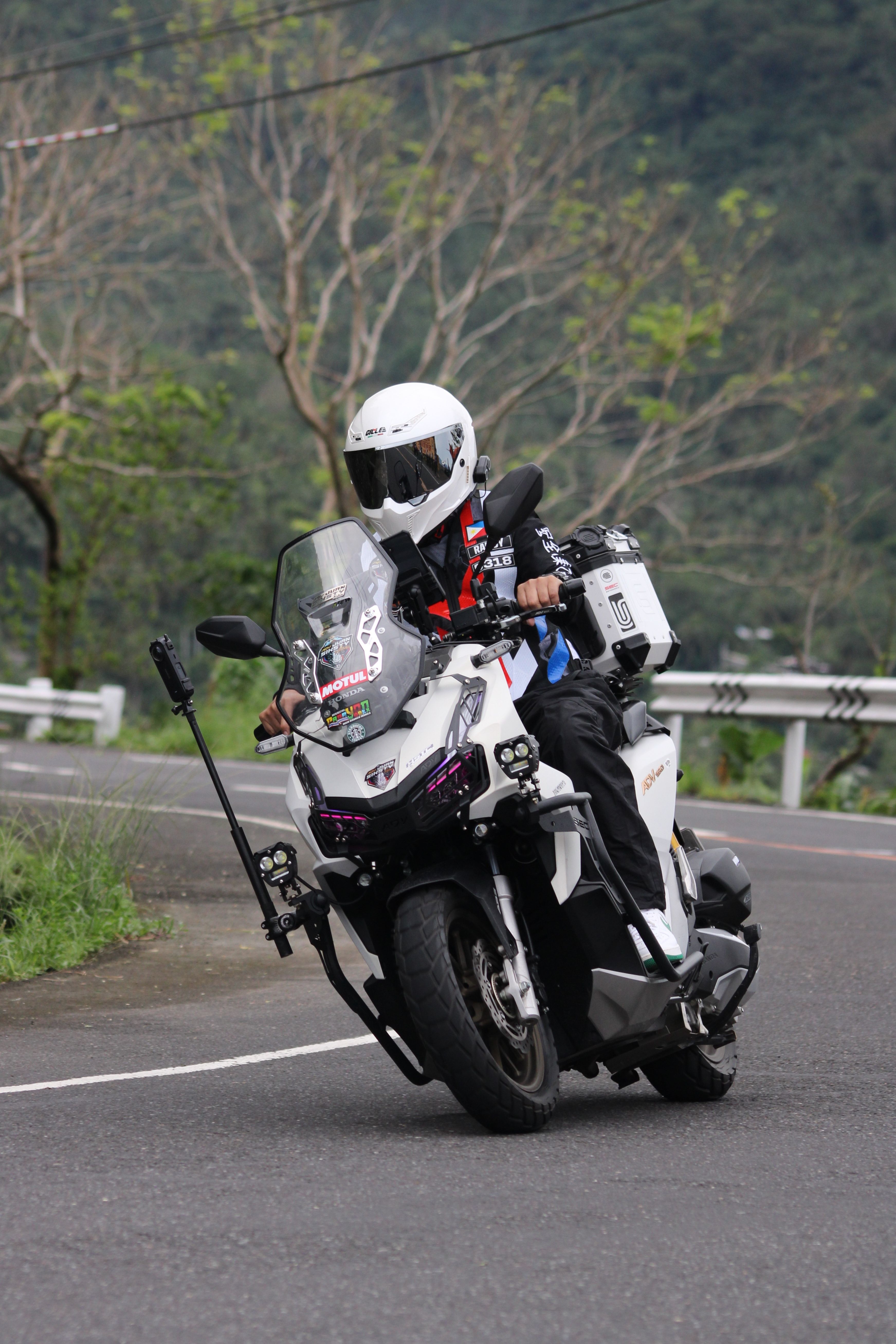 Motorcyclist in protective gear rides downhill on a lush, scenic mountain road.