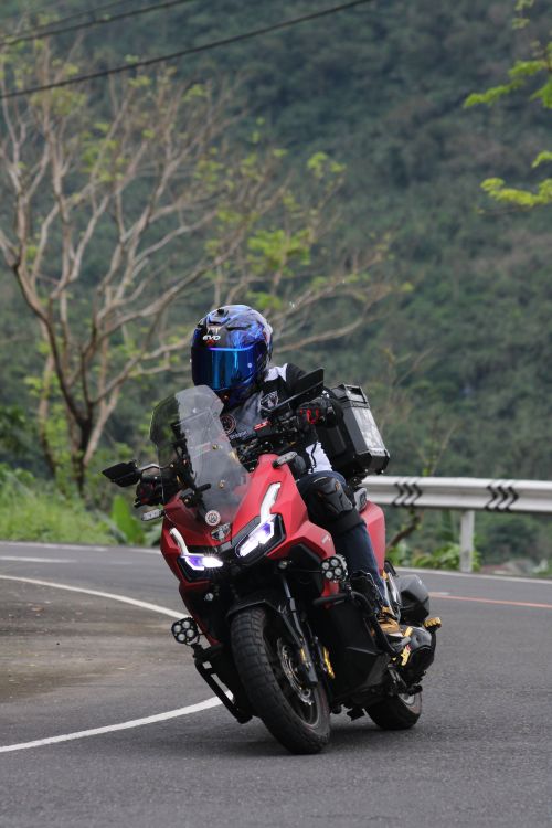 Free Motorcyclist in blue helmet riding a red touring bike on a winding mountain road. Stock Photo
