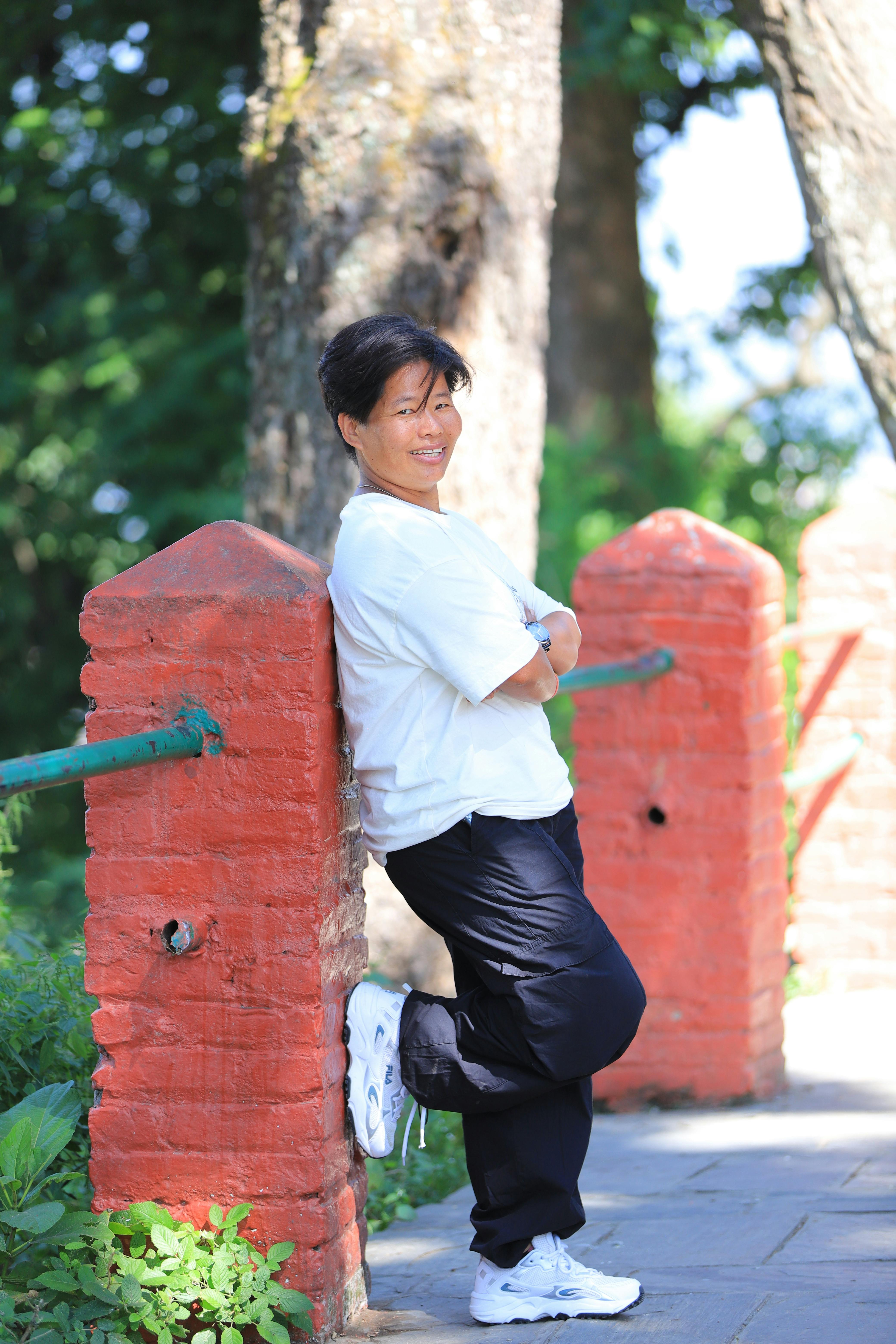Smiling person leaning on red brick wall outdoors on a sunny day.
