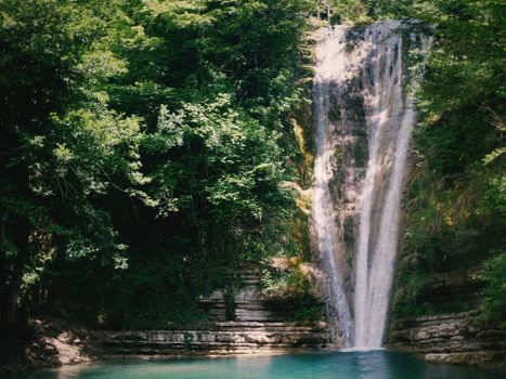 A serene waterfall cascading through lush greenery into a clear blue pool in a lush forest setting.