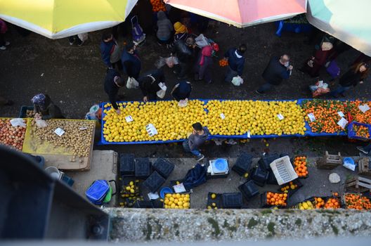 A busy outdoor market scene with tables filled with fresh lemons and oranges under colorful umbrellas.