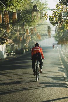Cyclist riding on a tree-lined road in Kon Tum, Vietnam during daytime.