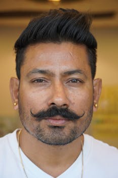 Close-up portrait of a man with a distinctive mustache and earrings, exuding confidence.