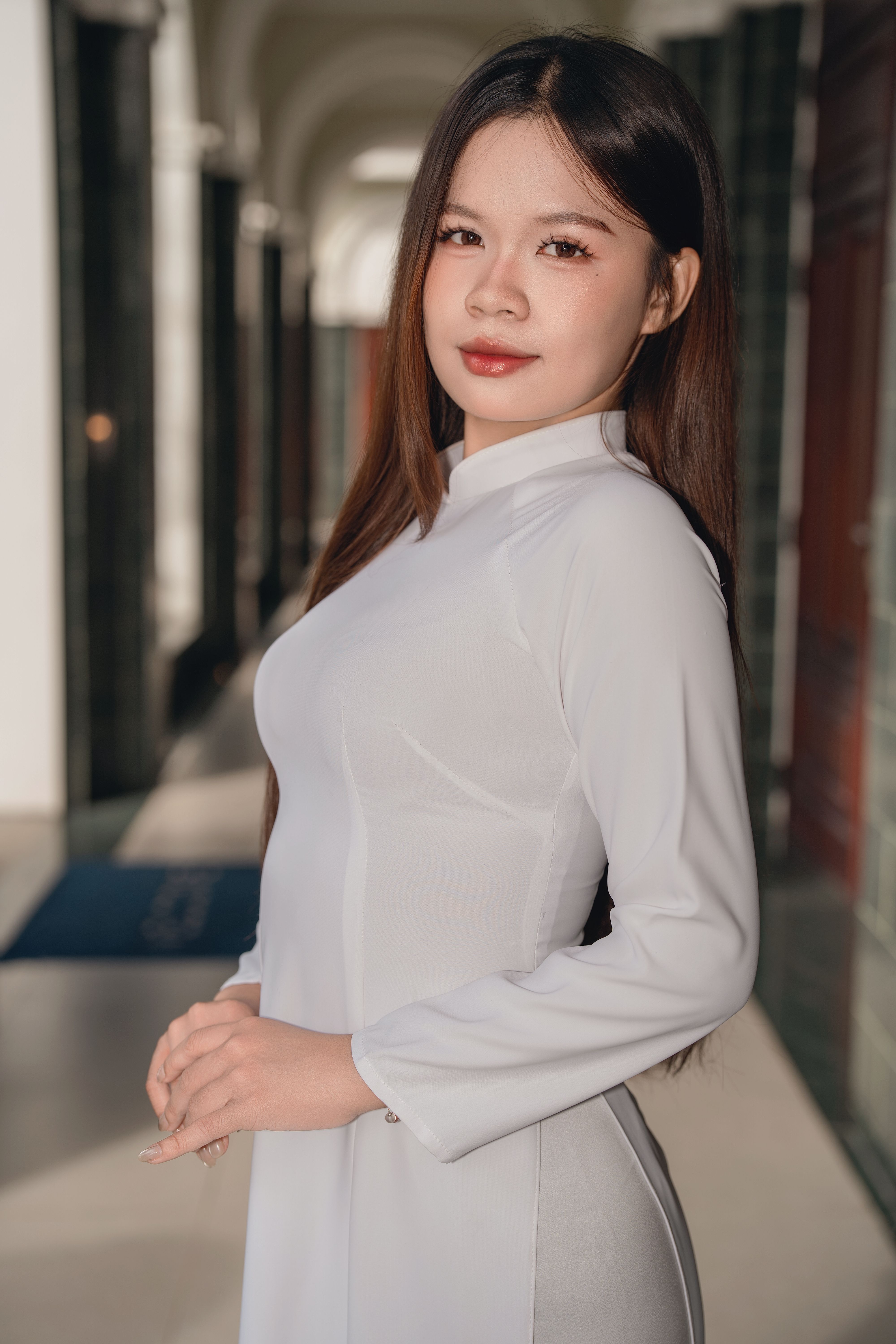 Young woman in white Ao Dai posing gracefully indoors with natural light.