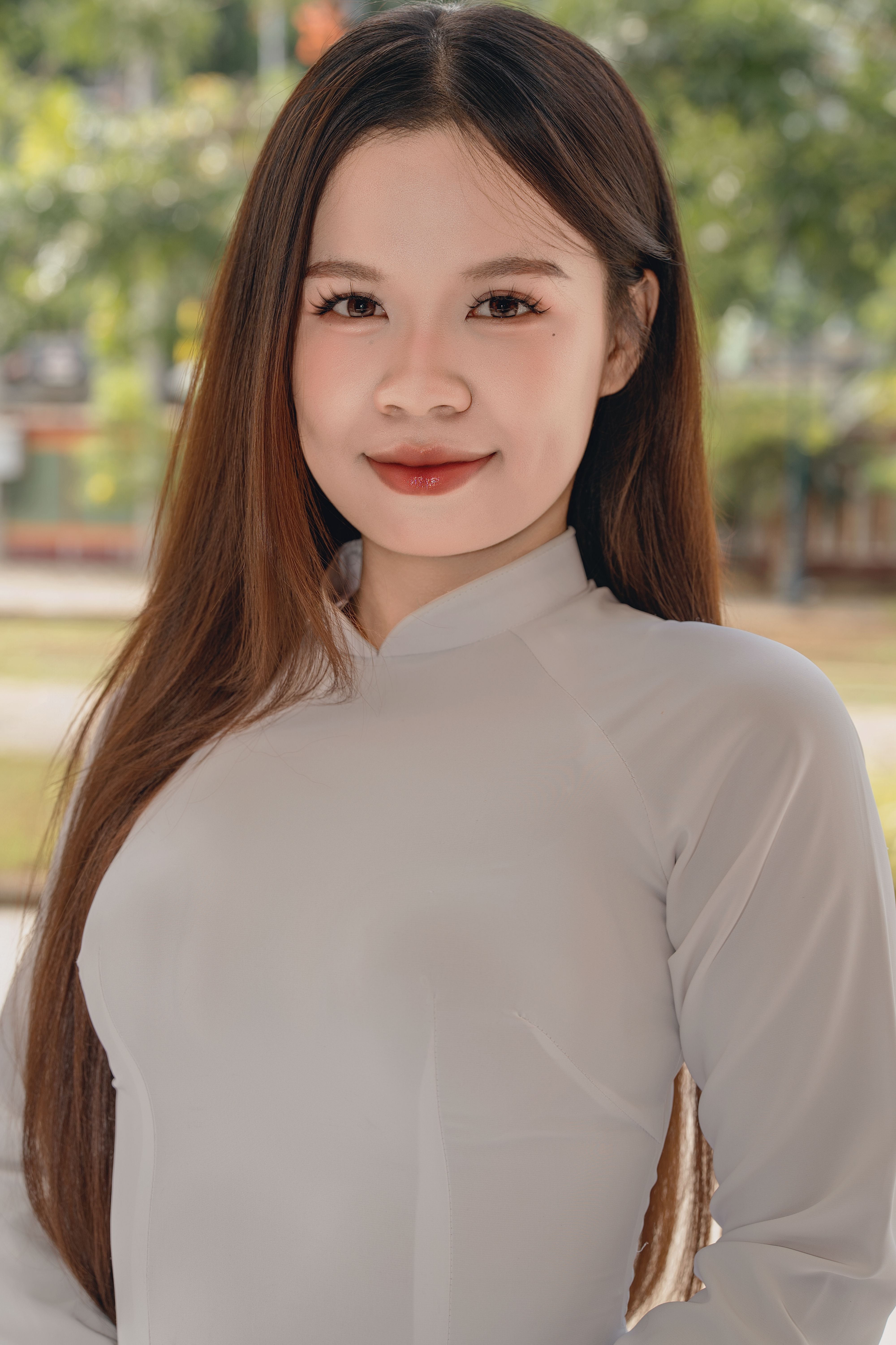 Close-up portrait of a woman smiling outdoors wearing a traditional white dress.