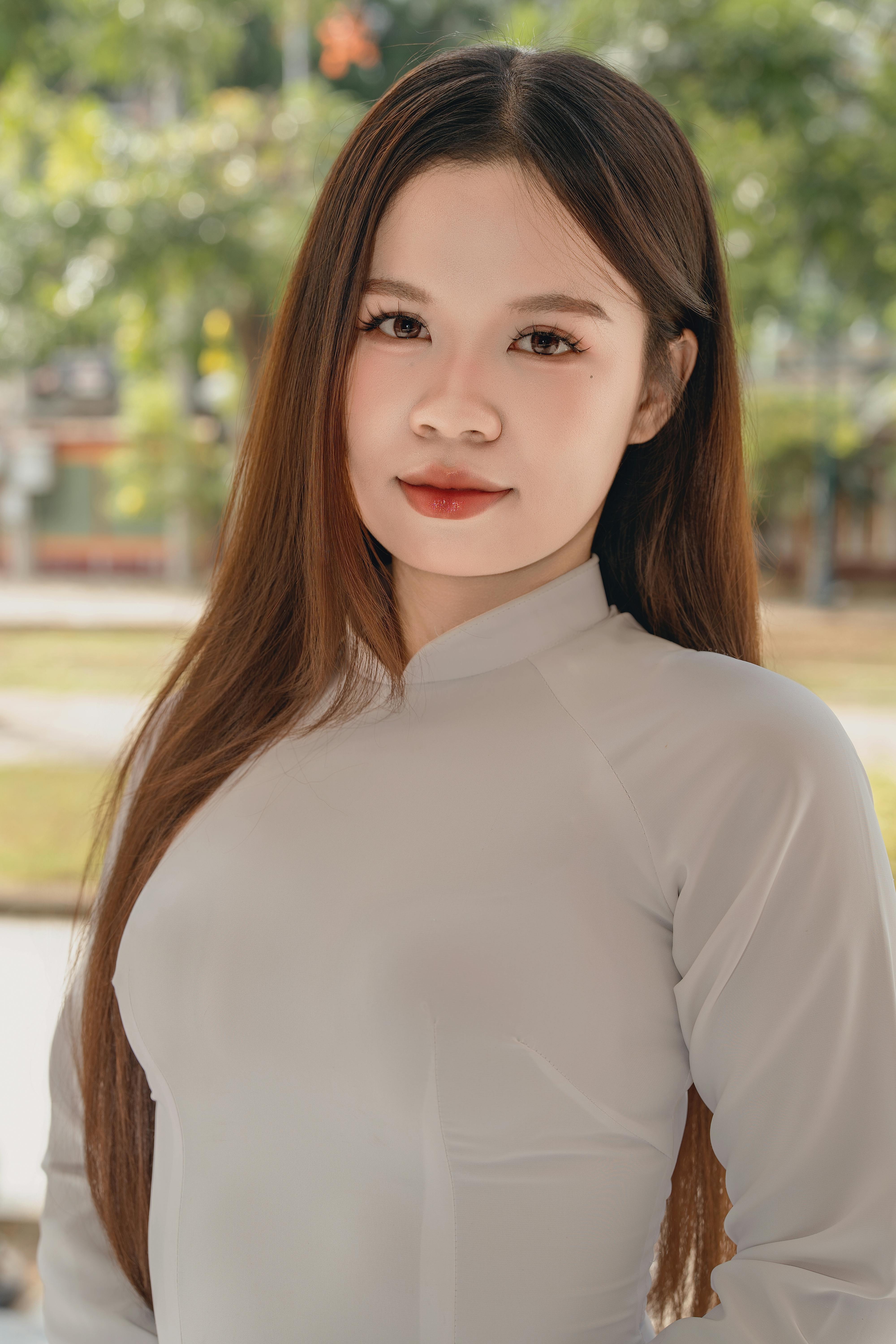 Portrait of a young woman in a white outfit, standing outdoors with a serene expression.